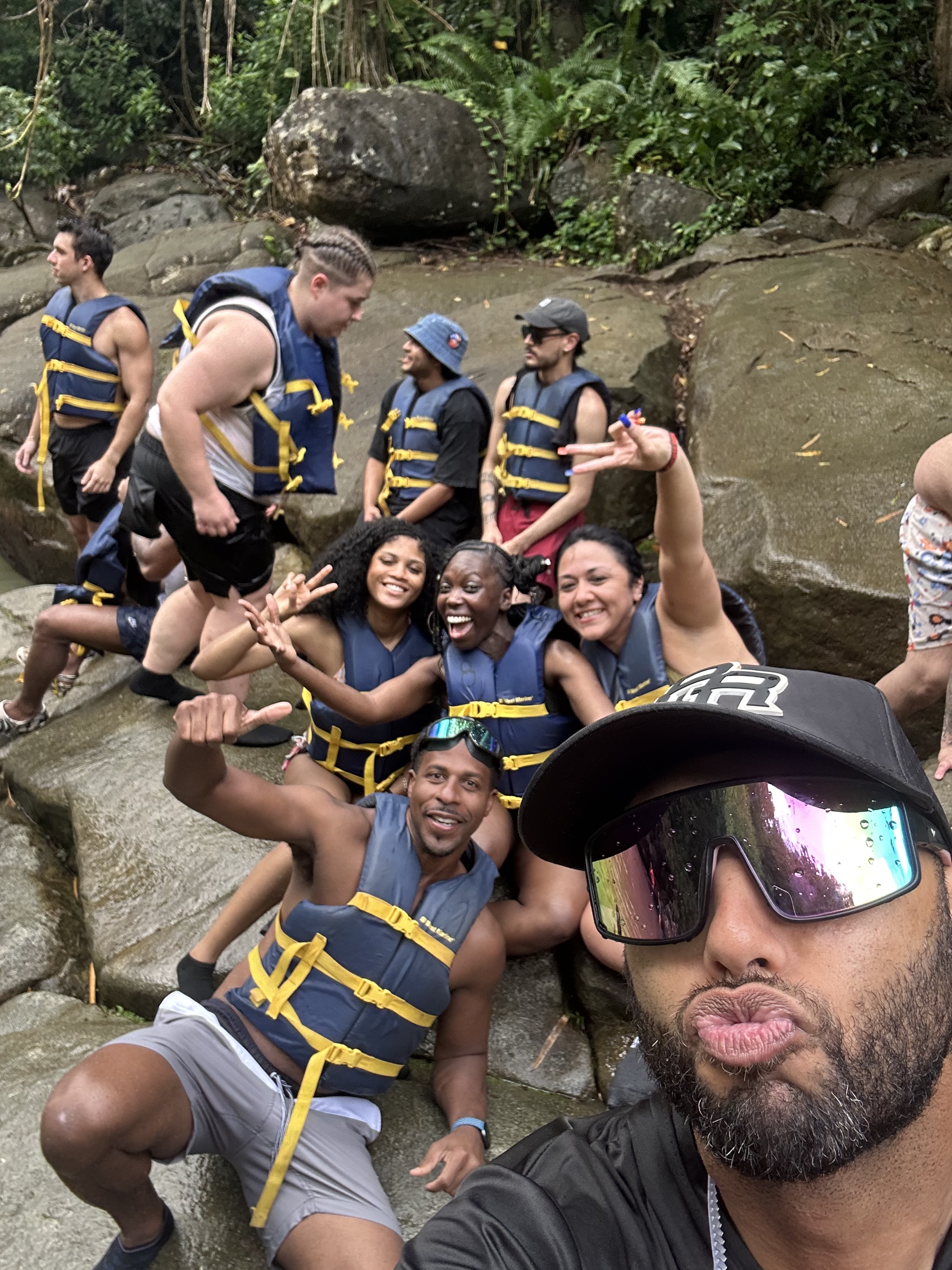 A photograph of a group of friends wearing life jackets, gathered among rocks in a lush forested setting.